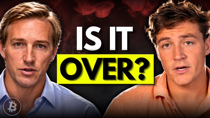 A YouTube thumbnail featuring two men against a dark, smoky red background with "IS IT OVER?" prominently displayed in the center and a Bitcoin logo in the bottom corner, promoting a live stream where 21Bullish and Mitchell Askew will discuss a pivotal Federal Reserve decision and its potential impact on the Bitcoin market.