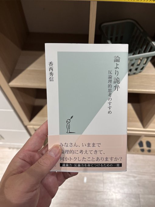 A hand holding a Japanese book by 香西秀信 (Hidenori Kozai) titled '論より詭弁 反論的思考のすすめ' (Persuasion over Argument) in a bookstore setting.