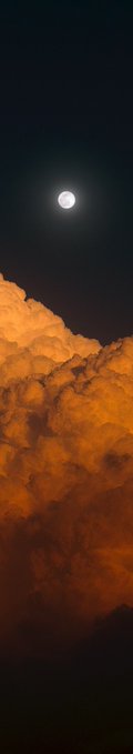A bright full moon glowing in the night sky above a thick bank of orange-lit clouds.