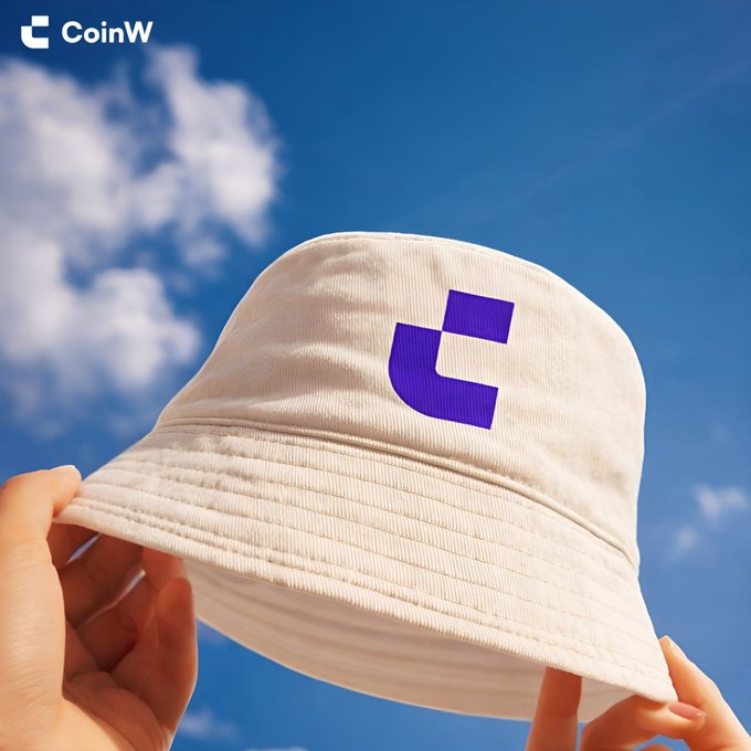 Two hands hold up a cream-colored bucket hat featuring a purple logo against a bright blue sky with white clouds, branded with 'CoinW' in the top left corner.
