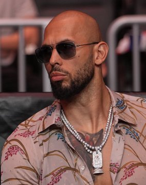 Andrew Tate, a bald man with a beard wearing sunglasses, a floral shirt, and a diamond chain pendant, is pictured as he reportedly made a $1.8 million deposit of $HYPE cryptocurrency to Binance, which was originally purchased for $550,000 two years prior.