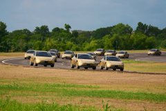 A row of white Tesla vehicles navigates a curved test track at an outdoor facility. The image's fleet of cars visually represents the post's vision of the Cybercab launching Tesla toward a $2,600 stock price.
