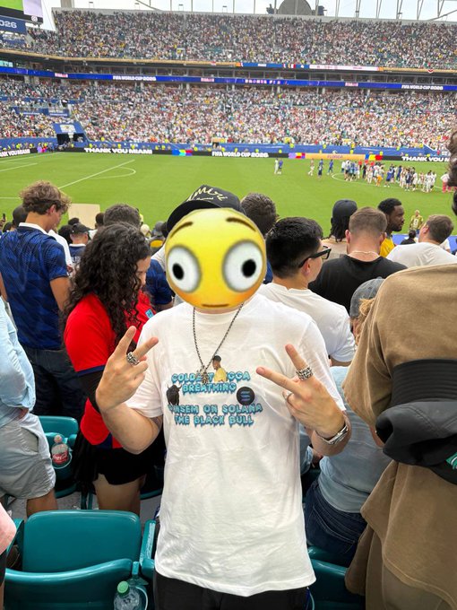 A fan at a stadium (FIFA World Cup branding visible) poses with peace signs while wearing a t-shirt reading "ONCE IN A LIFETIME / BASED ON SOLANA / THE BLACK BALL" and a cap that appears to say "MILF," fitting the post's celebration of an intense game tied to the $ANSEM crypto meme community.