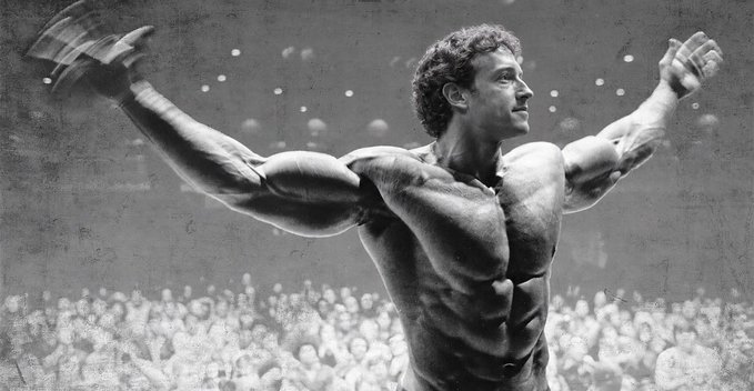 A grainy black-and-white image shows a highly muscular man, resembling a young Arnold Schwarzenegger in a bodybuilding pose, flexing both arms outwards on stage with a crowd visible below.