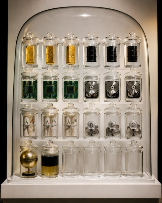 A wall-mounted display case features rows of glass jars containing various commodities—gold bars, hard drives, circuit boards, hard disk drives, oil derricks, steel rods, silver coins, a globe, and oil—alongside empty jars representing untapped markets. The curated arrangement visually represents the message "One account. Every Market," illustrating comprehensive access to diverse global asset classes within a single investment platform.