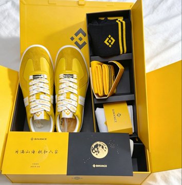 A yellow Binance merchandise gift box containing matching yellow sneakers, lanyard, wallet, and cards, branded with the Binance logo.