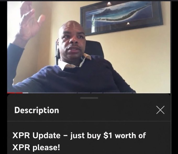 A man wearing a dark sweater gestures with his hand while speaking on a video call, with a framed artwork visible on the wall behind him. The video player displays a description reading "XPR Update – just buy $1 worth of XPR please!" The image connects to the post by showing the speaker delivering that XPR (Metallicus) update, referencing the #XPR and #MOVETOMETAL campaign and tagging Marshall Hayner.