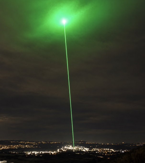 A vivid green laser beam shoots from a nighttime cityscape into cloudy skies. The post promotes an imminent “CA” drop and boldly predicts another “100x,” with the laser visually reinforcing the hype.