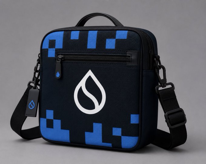 A black and blue pixel-patterned shoulder bag featuring a white water droplet logo, with an adjustable strap and zippered compartments. The water droplet design subtly mirrors the Sui Network branding referenced in the post, tying the accessory to the blockchain theme.