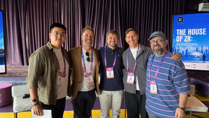 A group photo of five smiling men wearing conference badges at 'THE HOUSE OF ZK: INSTITUTIONAL INTELLIGENCE ONCHAIN,' standing in front of a blue event banner.