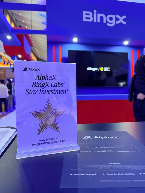 A promotional stand for AlphaX displayed at what appears to be a BingX-sponsored venue, highlighting 'AlphaX - BingX Labs' Star Investment' with a gold star design and website alphax.com.