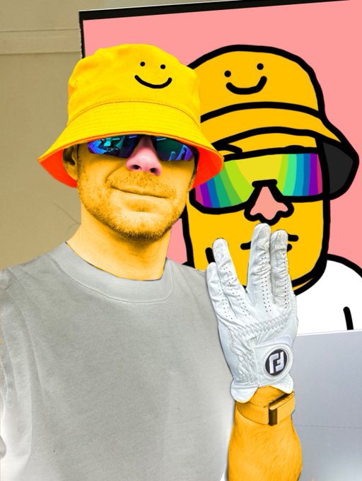 A person wearing a yellow smiley face bucket hat, reflective sunglasses, and a golf glove holds up a peace sign next to a cartoon character painting in the background.