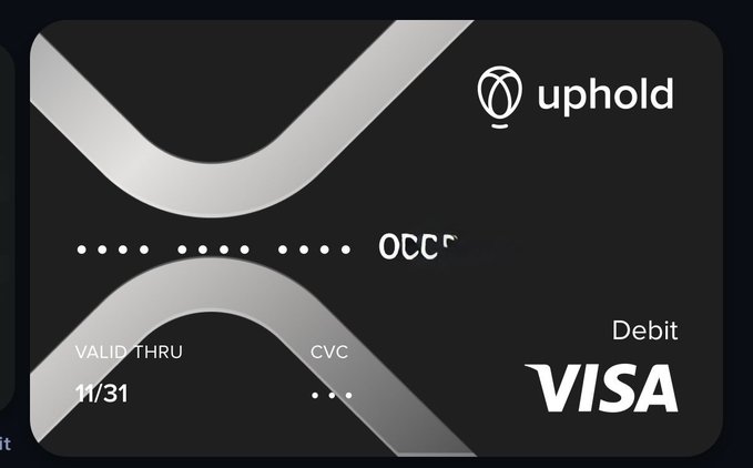A black Uphold Visa Debit card featuring a silver "X" design, displaying a masked card number starting with "0000," an expiration date of "11/31," and the Uphold logo in the top right corner, which corresponds to the @upholdinc handle.