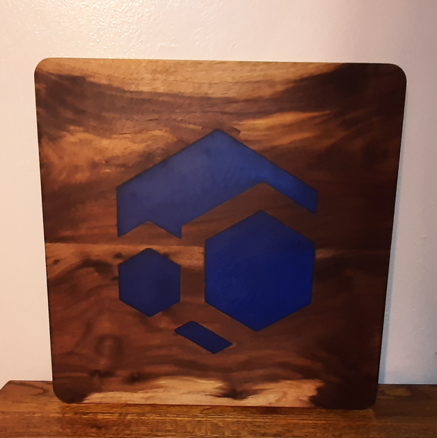 A wooden art board featuring blue geometric shapes including a hexagon, a chevron, and smaller geometric forms set against the natural wood grain.