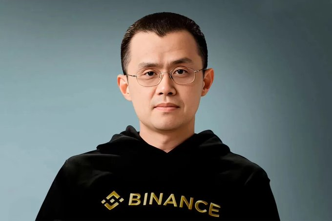 Portrait photograph of an Asian man wearing glasses and a black hoodie featuring the yellow Binance logo.
