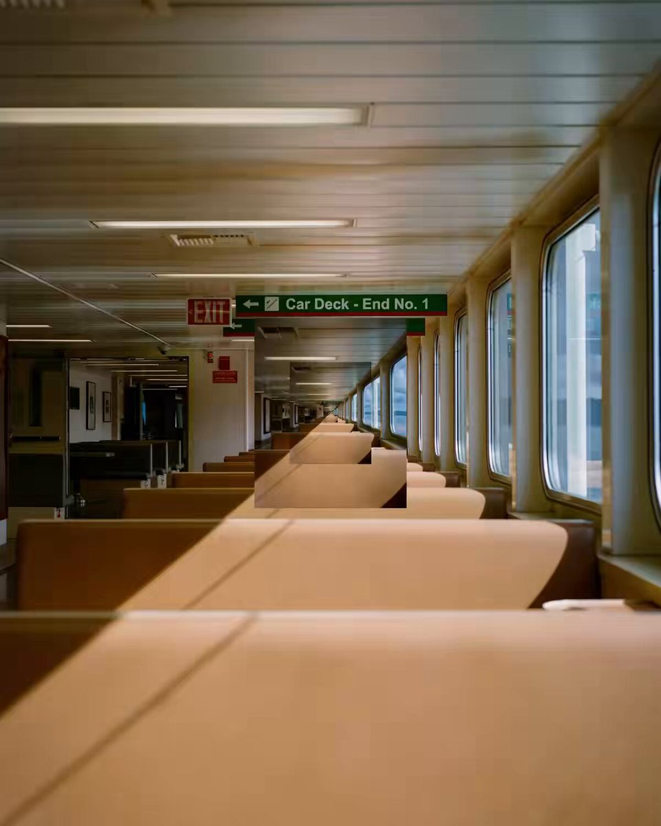 The image shows a long row of empty seats inside an airplane or train car. The seats are arranged in a straight line with no people visible. There is also a green sign hanging from the ceiling, which reads "Car Deck - End No." This suggests that this area is designated for passengers to wait before boarding their flight or train journey.
