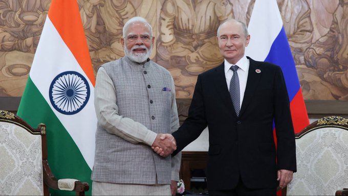 Indian Prime Minister Narendra Modi and Russian President Vladimir Putin shake hands during a bilateral meeting, with the Indian and Russian flags displayed behind them, highlighting diplomatic ties as the two nations explore using digital currencies for bilateral trade payments.
