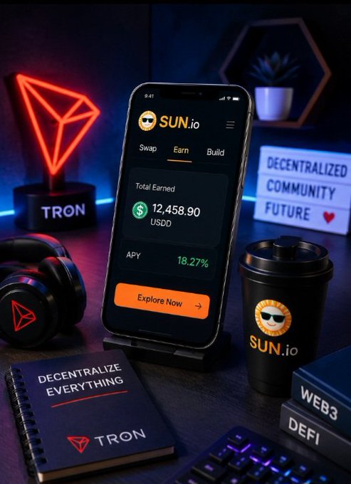 A promotional setup displays a smartphone showing the SUN.io app with 'Total Earned $12,458.90 USDD' and 'APY 18.27%', alongside a glowing TRON logo, a SUN.io branded tumbler, and signs reading 'DECENTRALIZE EVERYTHING' and 'DECENTRALIZED COMMUNITY FUTURE'.