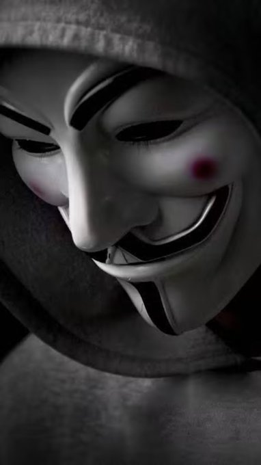 A person in a hooded sweatshirt wears a Guy Fawkes mask, evoking themes of anonymity, secrecy, and hidden truths that align with the post's message about concealed systems and a forthcoming revelation.
