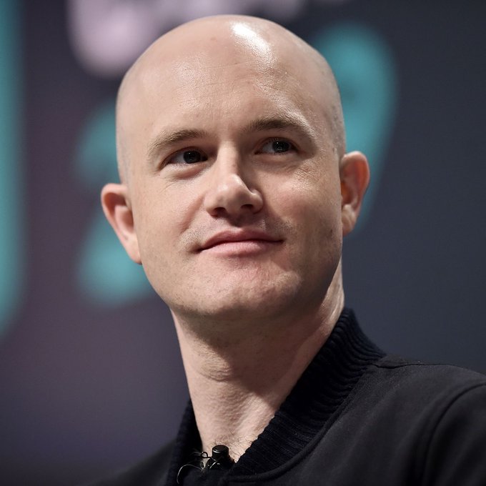 Coinbase CEO Brian Armstrong looks on with a subtle smile during an interview, pictured against a teal-toned stage backdrop. His composed demeanor contrasts with the breaking news that his company is pushing to expand into perpetual stock trading in the U.S., marking a bold move into derivatives.