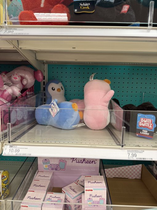 A retail store shelf displaying plush toys, including a pink Squishmallow priced at $7.99 and blue penguin plushies, with Pusheen-themed Gund merchandise on the lower shelf.