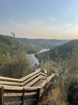 A wooden viewing platform overlooks a serene river winding through a forested canyon, emphasizing the peaceful escape from the crypto hustle. The image humorously contrasts this tranquil nature scene with the post's note about missing the "Arc" memecoin launch, suggesting that missing out on the trade led to a much-needed retreat into the great outdoors.