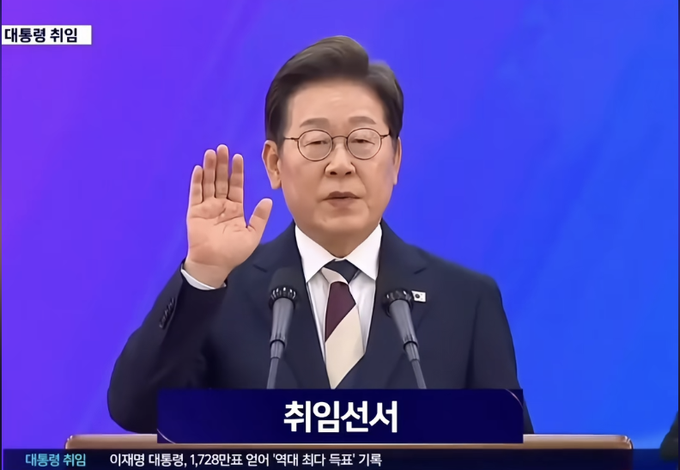 A man in a dark suit and glasses raises his hand while speaking at a podium labeled '취임선서' (Inauguration Oath), with the Korean text '대통령 취임' (Presidential Inauguration) visible on screen.