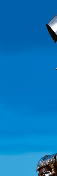 A dramatic upward shot of a blue sky with a metallic, ribbed object resembling the Sydney Opera House shell visible in the lower right corner.