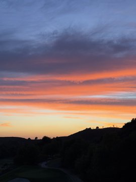 A vibrant sunset blazes with orange and pink hues over silhouetted mountain ridges and a darkening valley below, creating a peaceful "gn" (good night) scene to end the day.