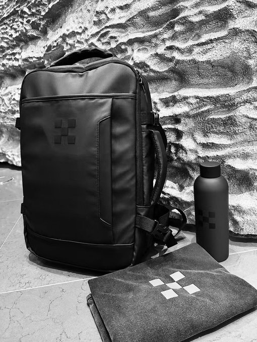 A sleek black backpack featuring the OKX logo is displayed alongside a matching black water bottle and a folded t-shirt, all branded with OKX branding. The promotional merchandise ties into the post's giveaway, offering crypto traders on Twitter an exclusive prize for sharing why they choose OKX for trading.