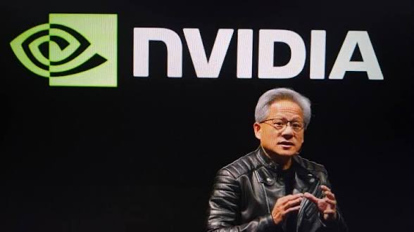 Jensen Huang, the CEO of NVIDIA, speaks on stage with the green NVIDIA logo displayed on a large screen behind him.