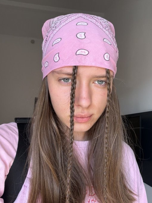 Selfie of a young person wearing a pink paisley bandana, with two braids framing their face, wearing a light pink top.