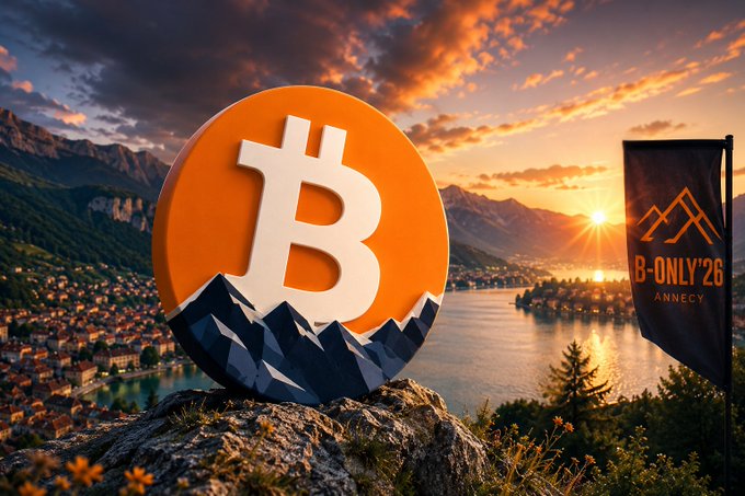 A large orange Bitcoin coin with mountain silhouettes rests on a rocky cliff overlooking a lake and town at sunset, next to a banner reading 'B-ONLY '26 ANNECY'.