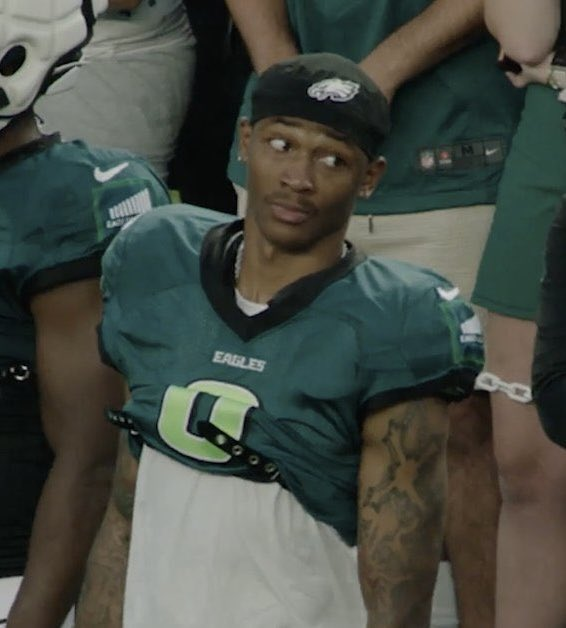 A young football player wearing an Eagles jersey with the letter 'C' and a cap poses sideways, looking at the camera.
