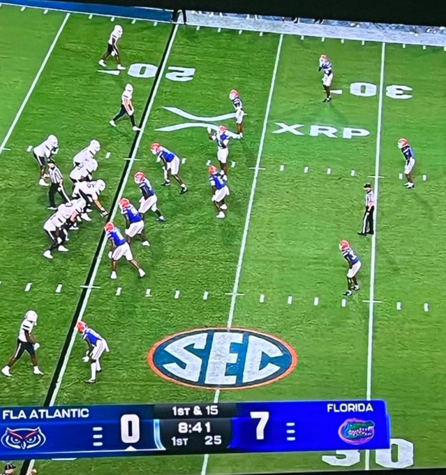 A college football game between Florida Atlantic and Florida, with Florida leading 7-0 in the 1st quarter with 8:41 remaining and a 1st & 15, showing players lined up on the field with an XRP logo painted at midfield and an SEC logo at the center.