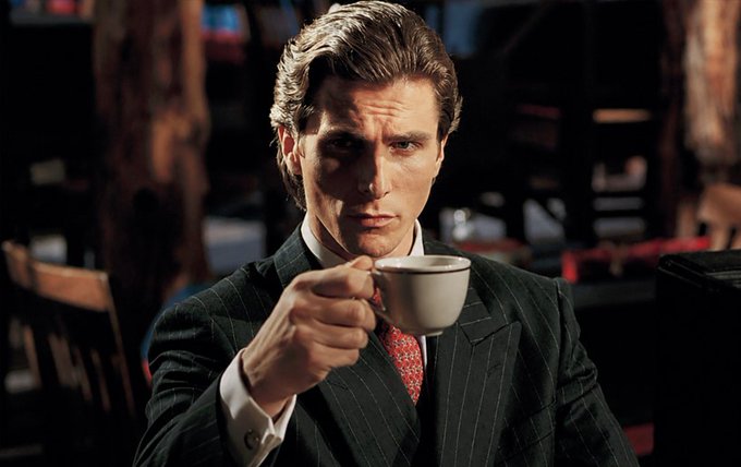 iced coffee with a red napkin, dressed in a dark suit and tie, seated at a table in a dimly lit restaurant.