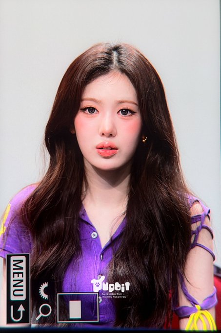 A young woman with long dark hair, wearing a purple collared shirt with cut-out sleeves, poses for a photo with a "MENU" button and "KiiiKiii" watermark visible on screen. The image appears to be a pre-debut or promotional shot of Sui from the K-pop group KiiiKiii, dated August 23, 2026.