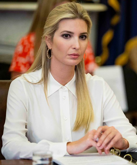 Ivanka Trump sits at a table wearing a white blouse and large hoop earrings, with long blonde hair, appearing to be in an official meeting setting.