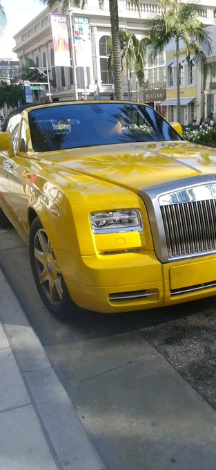 The image features a bright yellow Rolls Royce car parked on a city street. The car's shiny exterior and large hood suggest that it is well-maintained and possibly used for special occasions or events, such as weddings or parties. The photo captures the attention of viewers with its vibrant colors and unique design.