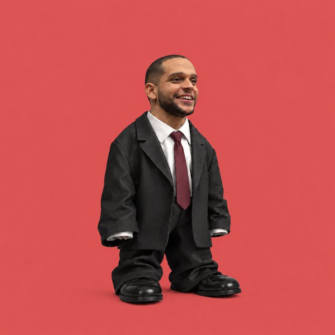 A surreal digitally manipulated image showing a tiny, chibi-style figure with a smiling man's head, wearing a loose black suit and red tie, set against a solid red background.