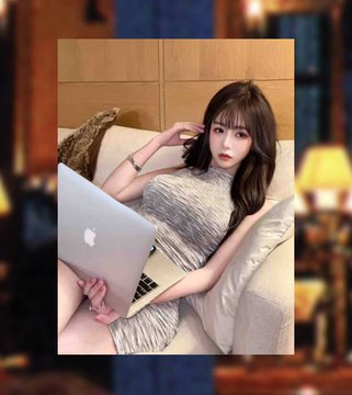 A young woman with dark hair reclines on a beige couch, holding an Apple MacBook laptop, with a blurred background suggesting a warmly lit interior.