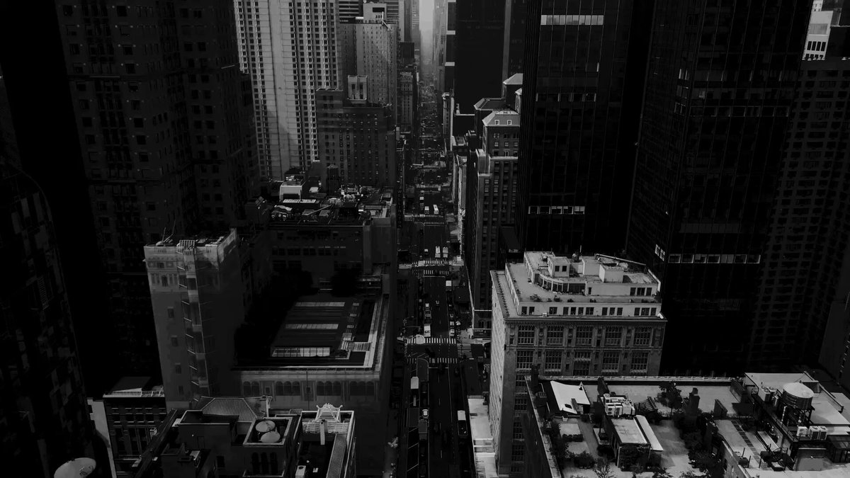 The image shows an aerial view of New York City's skyline during daybreak. The cityscape features tall buildings, including skyscrapers that dominate the scene. One of these structures has a "Newton" sign on its facade, indicating its connection to the field of physics or engineering. The photo is taken from a high vantage point, providing an expansive view of the city's architectural diversity and urban landscape.