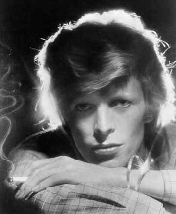 Black and white portrait of a young man with wavy blonde hair, resting his chin on his hands while holding a cigarette, with smoke drifting in the background.