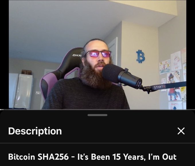 A bearded man with glasses sits in a DXR gaming chair speaking into a microphone, with a Bitcoin logo on the wall behind him; the video title reads "Bitcoin SHA256 - It's Been 15 Years, I'm Out."