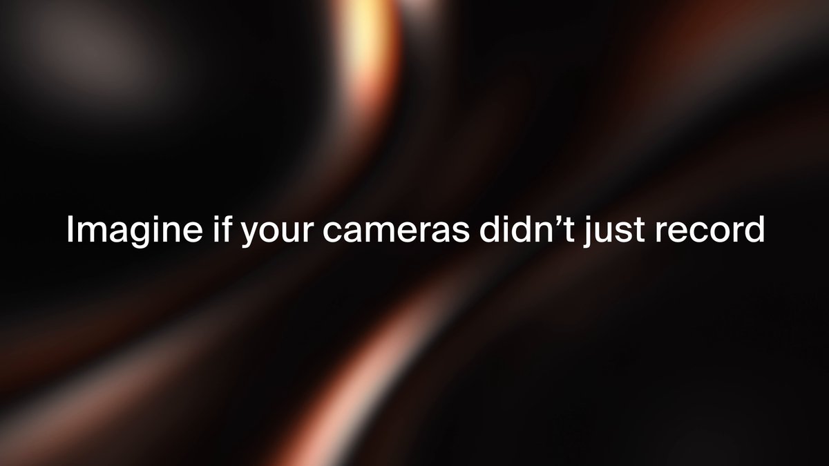 The image features a dark background with a large, blurry, orange-like shape that appears to be a camera lens or an object emitting light. The text "Imagine if your cameras didn't just record" is written above this shape. This suggests that the image could be related to a discussion about the limitations of current camera technology and how it affects our ability to capture images in various lighting conditions, such as low-light situations.