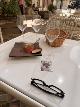 A restaurant table setting with two empty wine glasses, a bread basket, a small dish of sauce, and a pair of black eyeglasses on the white tabletop.