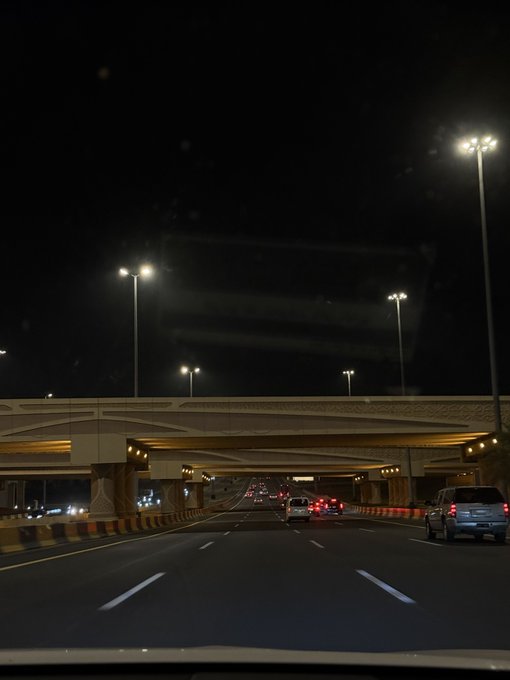 A nighttime dashcam view captures the drive on a multi-lane highway, with a partially legible dark billboard overhead and a few cars traveling under bright streetlights. The image complements the "happy friday" sentiment by sharing the relaxing late-night commute home.