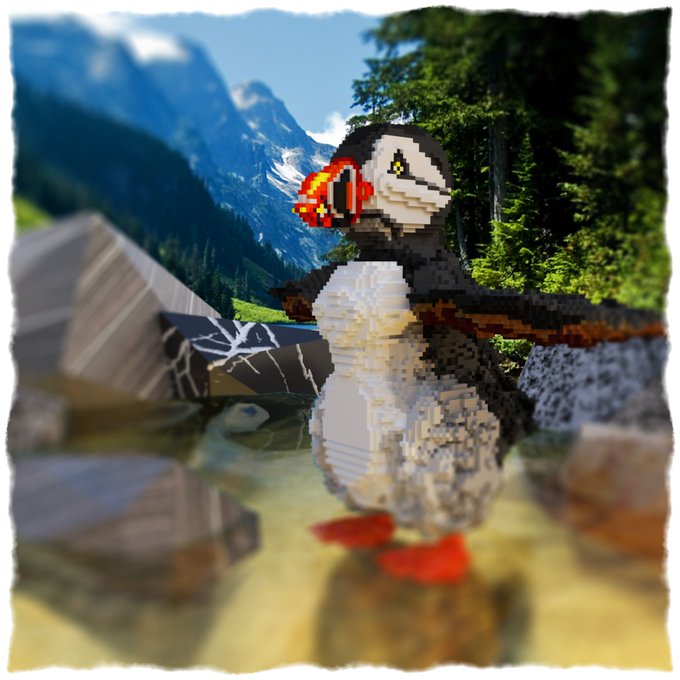 A voxel-style 3D puffin statue with a colorful orange and yellow beak stands in a scenic alpine landscape with mountains and a small waterfall, with its reflection visible in the water below. The image visually represents the unique 1-of-1 NFT art piece minted on Ethereum in April 2020, bringing the digital sculpture to life within a picturesque natural setting.