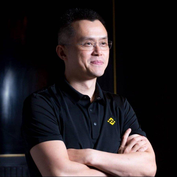 A smiling man wearing glasses and a black polo shirt with the Binance logo stands confidently with his arms crossed against a dark background. The image accompanies news about Changpeng Zhao (CZ), Binance's CEO, discussing how the exchange's market share growth stems from protecting and retaining its users.