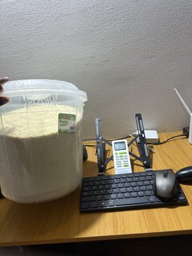 A desk setup featuring a large clear container of oats next to a cordless phone, keyboard, and mouse.